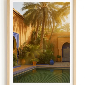 Peut inclure: Tirage encadré d'une scène de cour paisible. Des palmiers projettent des ombres sur une piscine aux carreaux verts et bleus. Les murs sont d'une teinte orange chaude, avec des accents bleus sur les portes et les pots. La scène est baignée de soleil.
