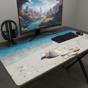 Puede incluir: Una alfombrilla de escritorio rectangular larga con una escena de playa con arena blanca, agua turquesa y conchas marinas. Un teclado, un ratón y un monitor negros están sobre el escritorio. Un auricular descansa sobre un soporte a la izquierda.