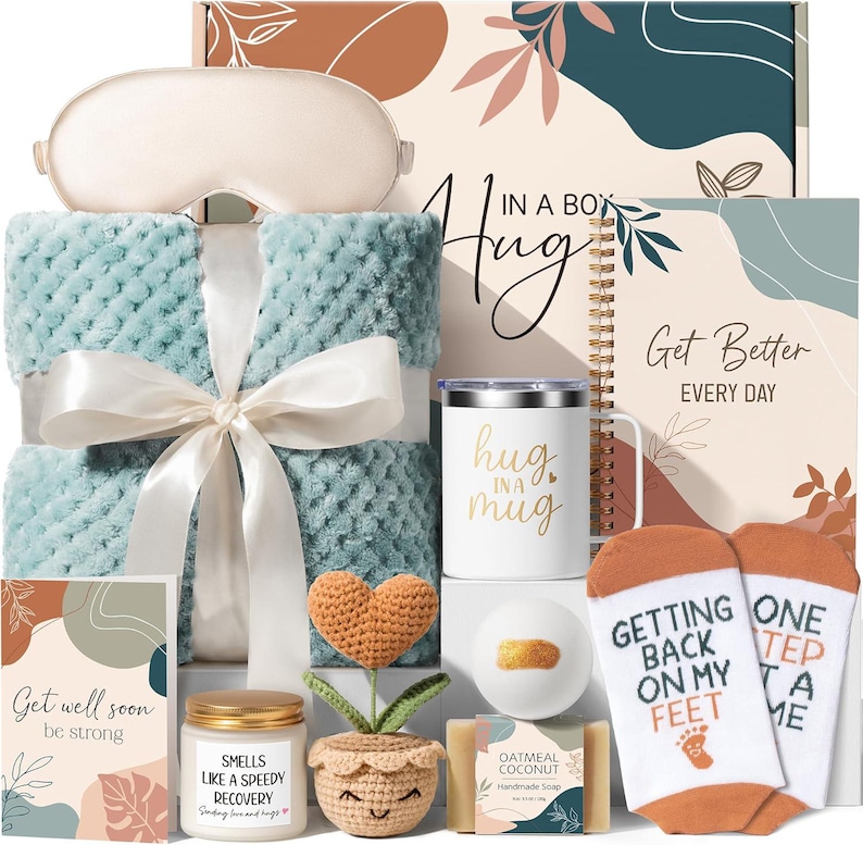 May include: A gift set containing a light blue textured blanket with a white ribbon, a beige sleep mask, a white mug with "hug in a mug" text, a spiral notebook with "Get Better EVERY DAY" text, socks with "GETTING BACK ON MY FEET" text, a candle, a crochet heart plant, a bath bomb, and soap.