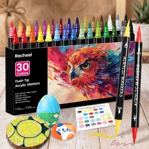 May include: A set of 30 Recheel dual-tip acrylic markers in a black box featuring an owl illustration. The set includes a colour chart card, a blue painted egg, a painted wooden slice with lime segments, and a small painted stone with a cat design.