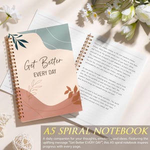 May include: A spiral-bound notebook with a cover featuring abstract shapes in sage green, cream, and terracotta, with the text Get Better EVERY DAY. The open page displays printed text, and the notebook is accented with gold-toned metal spiral binding.