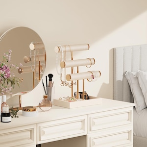 May include: A white vanity table with a round mirror and a gold jewelry display stand. The stand holds necklaces, bracelets, and rings. Other accessories include perfume bottles, makeup brushes, and a small tray of jewelry.