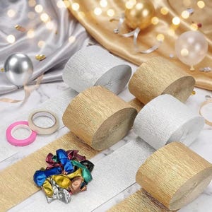 May include: A collection of party supplies including multiple rolls of metallic gold and silver crepe paper streamers, two rolls of adhesive tape in pink and white, and a pile of small, uninflated metallic balloons in various colors.