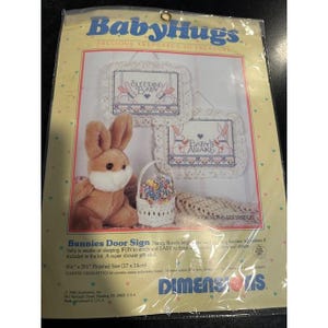Op de afbeelding: Baby Hugs kruissteekpakket met een pluche konijn, een bloemenmand en twee deurborden met de tekst "Sleeping Baby" en "Baby's Awake". Afmeting: 17 x 14 cm.