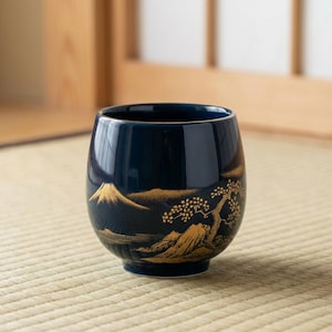 Peut inclure: Une tasse à thé en céramique bleu marine avec un motif doré de montagne et d'arbre. La tasse a une forme arrondie et une finition brillante. Le motif représente une chaîne de montagnes et un arbre.