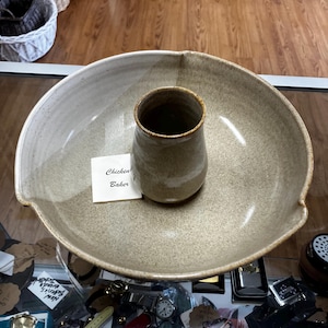 以下が含まれることがあります： 薄茶色の釉薬を施した陶器製のチキンベイカー。ベイカーは、中央に小さく円筒形のインサートが付いた、大きくて浅い皿を持っています。「Chicken Baker」というテキストの小さなカードがベイカーの前にあります。