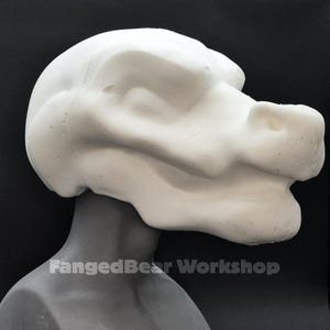 May include: A white, unpainted sculpted head of a creature with a snout and large ears. The head is mounted on a grey neck and torso form. The text "FangedBear Workshop" is printed at the base of the neck.