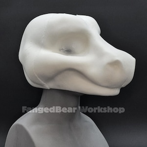 Könnte beinhalten: Ein weißer, unfertiger Fursuit-Kopf, geformt in einem Hunde- oder Reptilien-Stil. Der Kopf ist auf einem grauen Mannequinkopf montiert. Der Text "FangedBear Workshop" ist weiß am Halsansatz aufgedruckt.