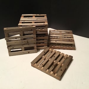 Puede incluir: Varias paletas de madera pequeñas y desgastadas están dispuestas sobre una superficie blanca contra un fondo negro. Las paletas rectangulares presentan un diseño de listones, mostrando signos de desgaste. La madera tiene un aspecto natural y envejecido.