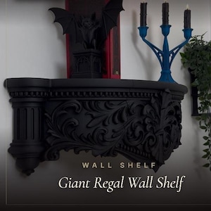 Puede incluir: Un estante de pared negro mate con intrincados tallados en volutas y un diseño de pilar estriado en el lado izquierdo. El estante sostiene un libro rojo, una figura de murciélago negra y un candelabro azul con tres velas negras. Texto: WALL SHELF Giant Regal Wall Shelf.