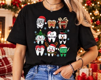 May include: A black short-sleeve t-shirt featuring a graphic print of nine cartoon teeth dressed in various Christmas-themed costumes, including Santa Claus, a gingerbread man, a gift, a tree, a snowman, and an elf, accented with snowflakes.