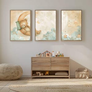 May include: Three framed watercolour prints with a nursery theme. One shows a teddy bear sleeping on a crescent moon. The other two depict clouds, stars, and moons in soft pastel colours. A wooden dresser and toys are below.