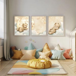 Peut inclure: Trois impressions encadrées représentant un ours en peluche sur une lune et des nuages. Les impressions sont dans un cadre de chambre d'enfant, avec des coussins colorés, un tapis et un pouf jaune. L'œuvre d'art a une palette de couleurs pastel.