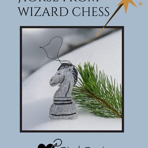 May include: A gray felt horse chess piece with black detailing, from a Wizard Chess set. The horse is displayed on a snowy surface with a sprig of green pine needles. The text "HORSE FROM WIZARD CHESS" is at the top.
