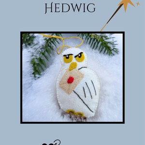 May include: A felt owl ornament with the name "HEDWIG" above it. The white owl holds a tan envelope with a red seal. The owl has yellow eyes and feet. The background is light blue with a star and a wand.