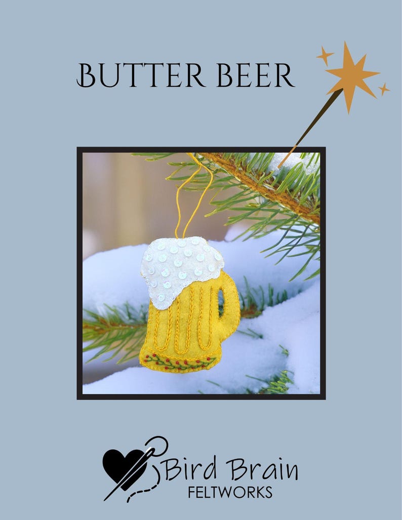 May include: A felt ornament shaped like a mug of butter beer, with a white foamy top and yellow body. The ornament is hanging on a pine branch with snow. The words "BUTTER BEER" are above the ornament.