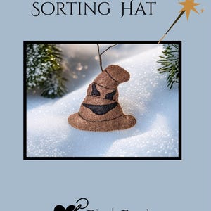 May include: A brown felt Sorting Hat with a black face design, displayed against a snowy backdrop. The image includes the text "SORTING HAT" and a logo for Bird Brain Feltworks. A gold wand with stars is also in the image.