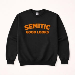 May include: Black sweatshirt with the words "SEMITIC GOOD LOOKS" printed in orange block letters. The sweatshirt has a crew neck and long sleeves. The text is centered on the chest.