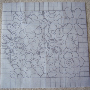May include: A black and white line drawing of a floral design on a gridded background. The design features various flowers, leaves, and swirls.