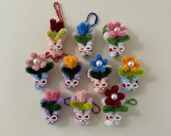 May include: A collection of handmade floral ornaments in various colors, including pink, blue, and orange. Each ornament features a pearl center and a small white bow. The ornaments are attached to a beaded chain or loop.