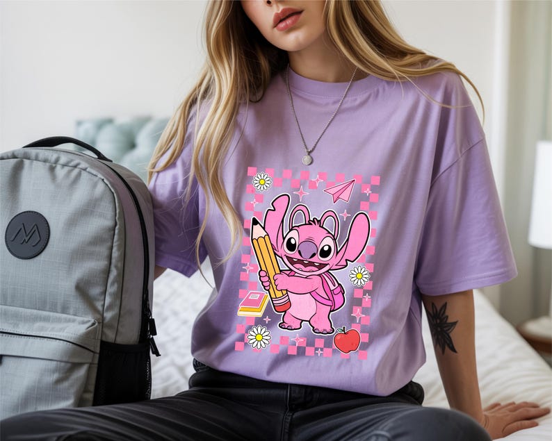 Może przedstawiać: Jasnofioletowy t-shirt z grafiką przedstawiającą r&oacute;żowego kosmitę trzymającego duży ż&oacute;łty oł&oacute;wek. Wz&oacute;r zawiera r&oacute;żowe tło w kratkę, czerwone jabłko, małą książkę, białe stokrotki oraz ikonę r&oacute;żowego papierowego samolotu.