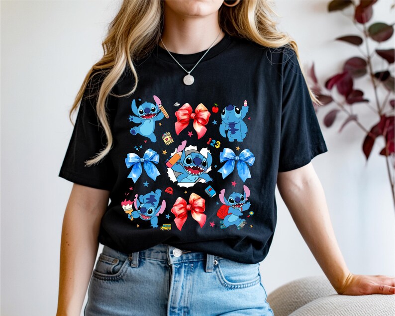 Op de afbeelding: Een zwart t-shirt met korte mouwen voorzien van een grafische print van het blauwe personage Stitch in verschillende houdingen, afgewisseld met rode en blauwe strikken, kleine sterretjes en schoolgerelateerde items zoals een potlood, een boek en de cijfers 123.