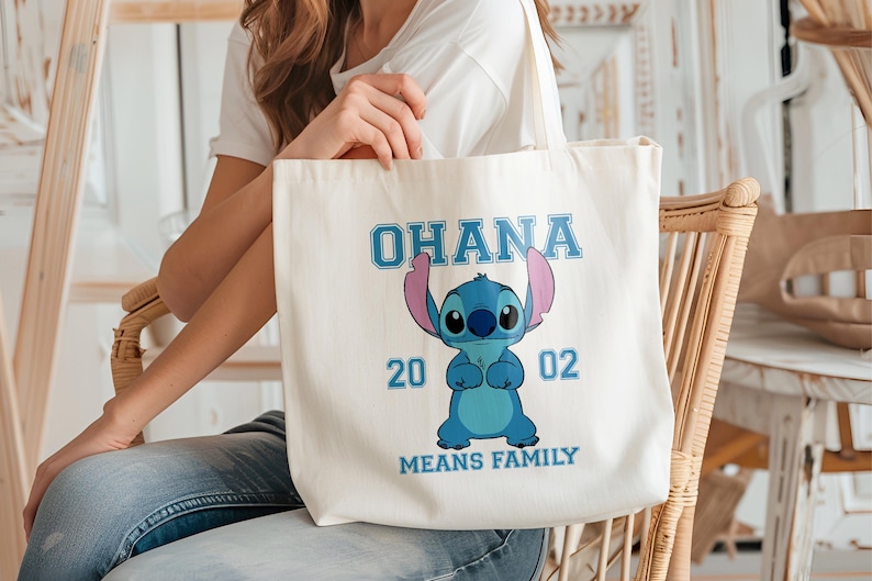 May include: Cream-colored tote bag featuring a blue cartoon character with large ears and the text "OHANA MEANS FAMILY". The character is in the center, with the numbers "20" and "02" on either side.