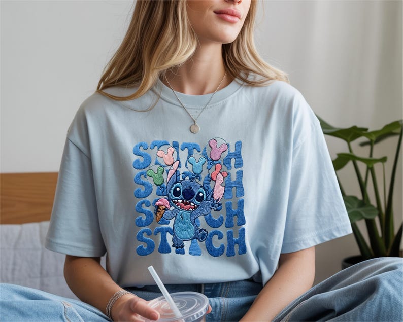 May include: Light blue t-shirt featuring the character Stitch from Lilo & Stitch. The design includes Stitch holding ice cream and balloons, with the name "STITCH" in a stacked, bubble-style font. The shirt is a casual, short-sleeved style.