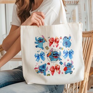 Op de afbeelding: Een witte canvas draagtas met een kleurrijke grafische print van het blauwe personage Stitch in verschillende houdingen, afgewisseld met rode en blauwe strikken, kleine sterretjes, een rode appel, een gele schoolbus en de cijfers 123.