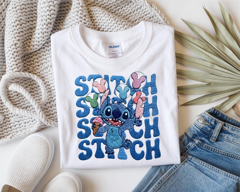 May include: White t-shirt featuring a blue Stitch graphic holding ice cream and balloons. The word "STITCH" is embroidered in blue. The shirt is paired with blue jeans and white sneakers.