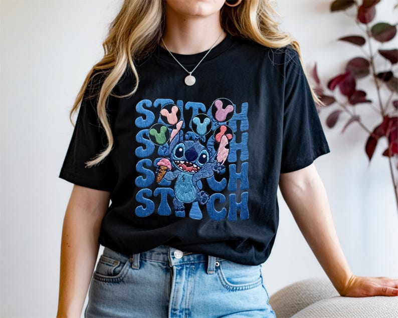 May include: Black t-shirt featuring a blue cartoon character holding an ice cream cone, with the word "STITCH" in blue block letters. The character is surrounded by colorful Mickey Mouse-shaped ice cream. The shirt is a casual, comfortable style.