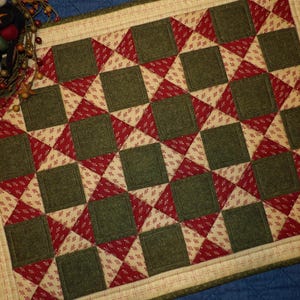 May include: A green and red patchwork quilt with a geometric pattern. The quilt is made of squares and triangles and has a cream-colored border.