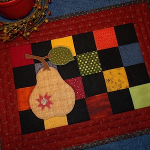 May include: A quilted wall hanging with a patchwork design featuring a variety of colors and patterns, including red, green, yellow, and black. A pear-shaped applique is centered on the wall hanging.