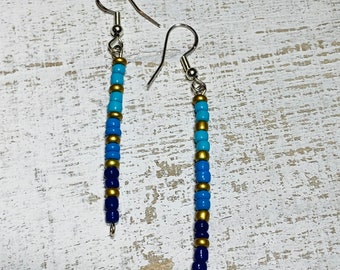 May include: A pair of dangle earrings with a gradient of blue and gold beads. The earrings are made with small, round beads that are strung together on a silver wire.