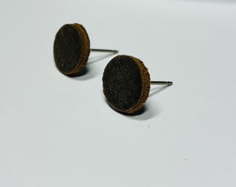 Könnte beinhalten: Zwei braune und schwarze Ohrstecker. Jeder Ohrring hat ein kleines, kreisförmiges, dunkelbraunes Filzpad mit einem helleren braunen Rand, das an einem silberfarbenen Stift befestigt ist. Die Ohrringe sind vor einem weißen Hintergrund platziert.