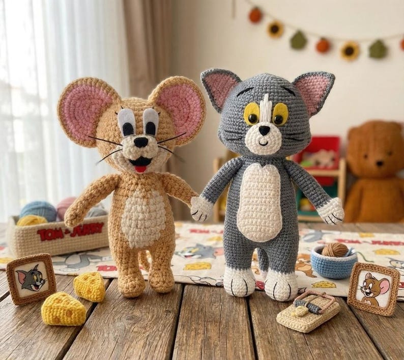 May include: Handmade crochet figures of Tom and Jerry, standing together. Jerry is beige with pink ears, and Tom is grey with a white patch. The scene includes crocheted cheese and a mouse trap, inspired by the cartoon.