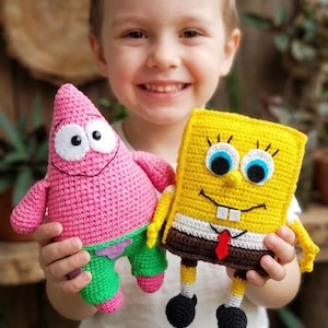 May include: Two handmade crochet plush toys: Patrick Star in pink with green shorts and SpongeBob SquarePants in yellow with a red tie. Both toys have black eyes and are held by a child. The toys are made of yarn.
