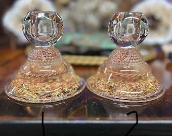 May include: Two clear glass candle holders with a decorative gold and copper base. The candle holders have a round, textured top and a flared base with gold flecks. The base is accented with copper wire.