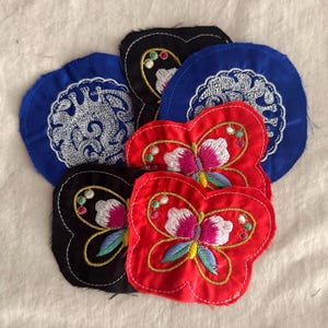 May include: A collection of embroidered patches in various shapes and colors. The patches include blue circles with white floral designs, black butterfly shapes with floral embroidery, and red butterfly shapes with colorful embroidery.