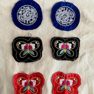 May include: Six embroidered patches in a variety of colors. Two blue circular patches with white floral designs, two black butterfly-shaped patches with colorful embroidery, and two red butterfly-shaped patches.