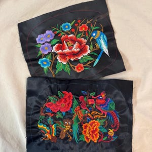 May include: Two black fabric patches with colorful embroidered floral and bird designs. One features a red peony, blue bird, and purple flowers. The other has a phoenix, owl, and butterfly with vibrant colors.