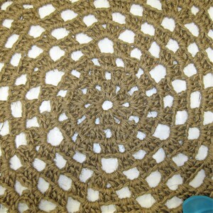 May include: A close-up of a brown crocheted round rug with a white background. The rug has a circular pattern with a center circle.
