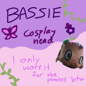 May include: A brown fabric headpiece featuring large circular eyes and a small mouth, topped with a colourful floral crown. The image includes the text BASSIE cosplay head and I only wore it for the photos btw, set against a purple and pink background.