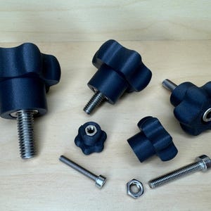 May include: Several black, star-shaped knobs with threaded bolts and a nut. The knobs are made of a dark, matte material. The bolts and nut are silver. The items are arranged on a light-coloured wooden surface.