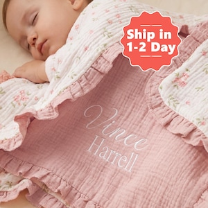 May include: A baby blanket with a pink and white floral pattern. The blanket has a ruffled edge and the name "Vince Harrell" embroidered in white script. The blanket is made of a soft, textured fabric.