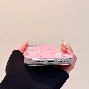 Pu&ograve; includere: Custodia per telefono rosa con bordo trasparente. La custodia presenta un motivo ripetuto di personaggi dei cartoni animati e fiori. La custodia &egrave; realizzata in un materiale trasparente e flessibile.