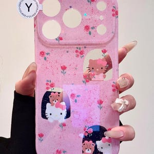 Pu&ograve; includere: Custodia per telefono rosa con finitura glitterata, con Hello Kitty e disegni floreali. La custodia ha ritagli per la fotocamera e il flash e include il testo "Hello Kitty".