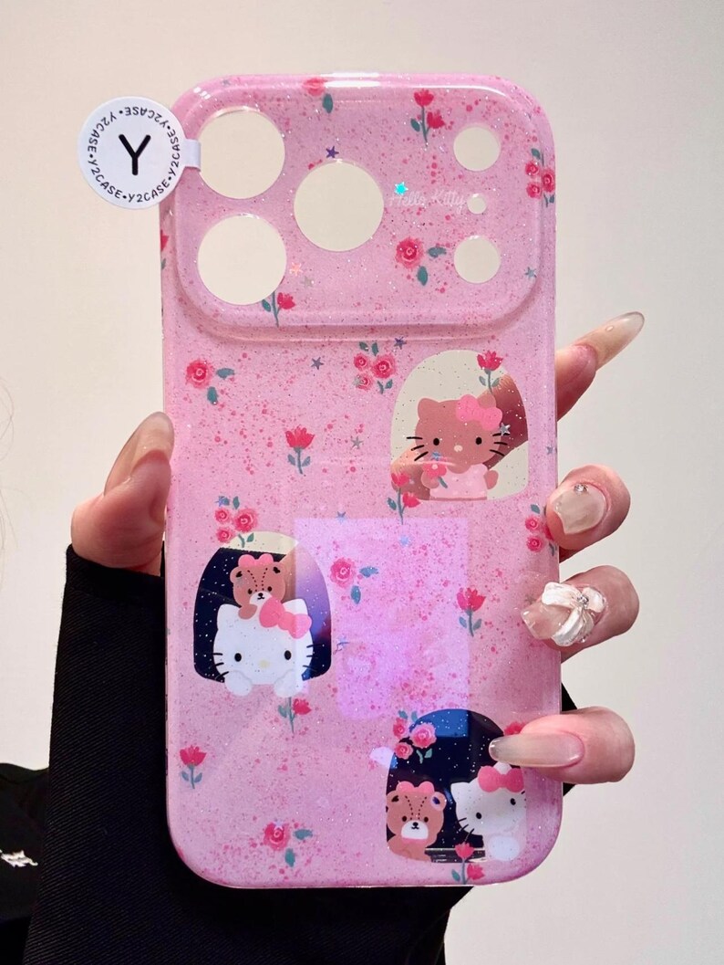 Pu&ograve; includere: Custodia per telefono rosa con finitura glitterata, con Hello Kitty e disegni floreali. La custodia ha ritagli per la fotocamera e il flash e include il testo "Hello Kitty".