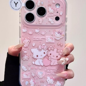 May include: Pink phone case with Hello Kitty illustrations. The case has a clear border and a pink interior with multiple Hello Kitty designs, bows, and the word "charming". The case has a Y2CASE sticker.