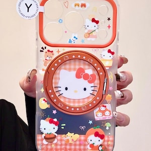 May include: Transparent phone case with a Hello Kitty design and an orange frame. The case features cartoon illustrations of Hello Kitty, stars, and food items. The design is set against a checkered background.
